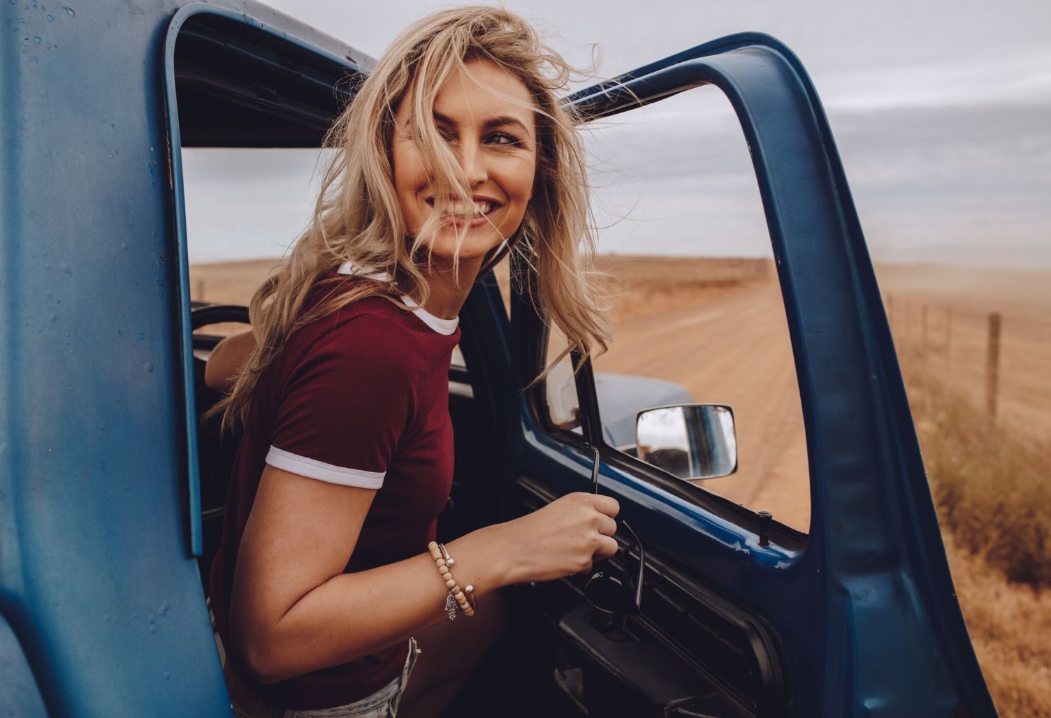 A driver smiling from the open door of a pickup truck on a desert road